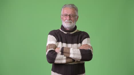 Handsome-senior-bearded-man-wearing-warm-clothing-against-green-background