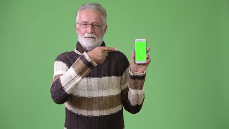 Handsome-senior-bearded-man-wearing-warm-clothing-against-green-background