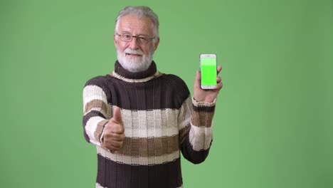 Handsome-senior-bearded-man-wearing-warm-clothing-against-green-background