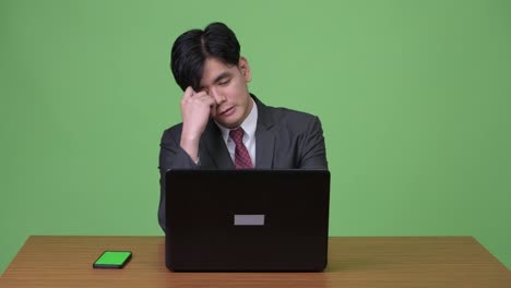 Joven-empresario-asiático-guapo-trabajando-con-ordenador-portátil-contra-el-fondo-verde