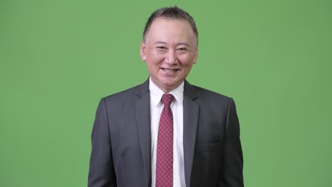 Mature-happy-Japanese-businessman-smiling-against-green-background