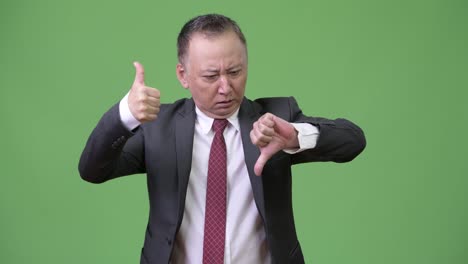 Mature-confused-Japanese-businessman-choosing-between-thumbs-up-or-thumbs-down