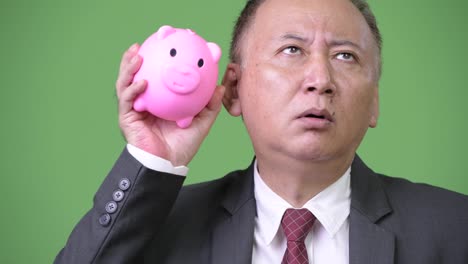 Mature-Japanese-businessman-holding-piggy-bank