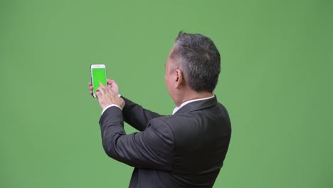 Mature-Japanese-businessman-showing-phone-to-camera