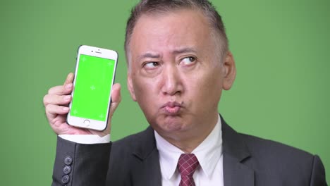 Mature-Japanese-businessman-showing-phone-to-camera