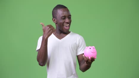 Young-African-man-holding-piggy-bank-and-giving-thumbs-up