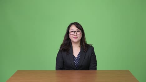 Mature-happy-beautiful-Asian-businesswoman-smiling-while-sitting-behind-desk