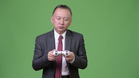 Mature-Japanese-businessman-playing-games-against-green-background