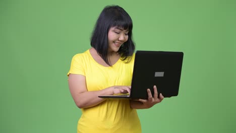 Schöne-glückliche-asiatische-Frau-denken-während-mit-laptop