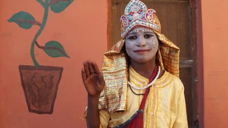 Young-girl-dressed-as-a-goddess-with-painted-face-gives-blessings-looking-towards-the-camera-with-one-hand-raised-handheld