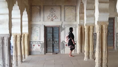 Frau-Tourist-herumlaufen-Säulen-Spalten-Innenarchitektur,-die-traditionelle-indische-Motiv-Türen-Stein-handgefertigte-ethnische-alte-Kunstdesign-einer-alten-mittelalterlichen-statische-Breite-Schuss-Sperre-nach-unten-Holz