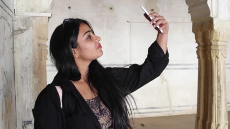 Pretty-woman-taking-photo-video-selfie-with-mobile-phone-camera-at-a-temple-old-ruin-building-interior-with-Indian-architecture-beautiful-handmade-admire-magnificent-handheld-arc-column-Rajasthan