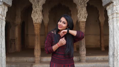 Gorgeous-young-woman-gets-good-news-wears-smart-watch-happy-thrilled-celebrate-fists-in-the-air-looks-at-camera-in-front-of-a-tradition-Indian-architectural-facade-Handheld-stabilized-mid-shot-learns