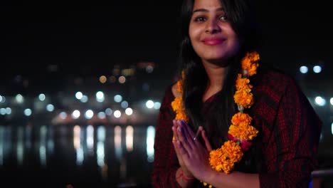 Beautiful-young-woman-hands-joined-in-namaste-greets-with-orange-marigold-flower-garland-on-her-neck-offers-prayers-worship-God-Goddess-hands-welcomes-smiles-glowing-respect-believer-religion-handheld