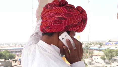 Close-up-of-Indian-man-hectic-on-a-cell-phone-conversation-on-a-rooftop-in-traditional-clothes-in-Rajasthan,-India