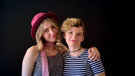 Two-happy-charming-women-hugging-and-smiling-at-camera,-isolated-on-black-background