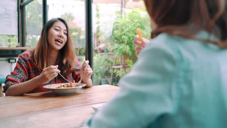 Beautiful-happy-Asian-women-lesbian-lgbt-couple-sitting-each-side-eating-a-plate-of-Italian-seafood-spaghetti-and-french-fries-at-restaurant-or-cafe-while-smiling-and-looking-at-food.