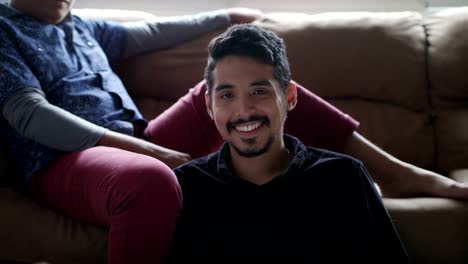 Hispanic-Gay-Couple-Holding-Hands-On-Sofa-at-Home