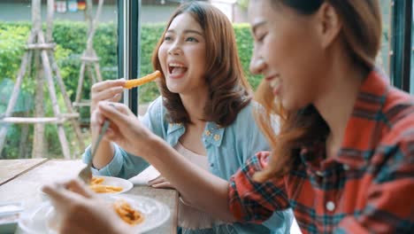 Beautiful-happy-Asian-women-lesbian-lgbt-couple-sitting-each-side-eating-a-plate-of-Italian-seafood-spaghetti-and-french-fries-at-restaurant-or-cafe-while-smiling-and-looking-at-food.