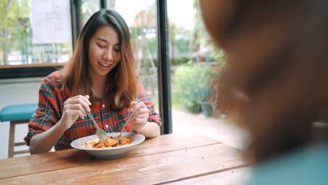 Beautiful-happy-Asian-women-lesbian-lgbt-couple-sitting-each-side-eating-a-plate-of-Italian-seafood-spaghetti-and-french-fries-at-restaurant-or-cafe-while-smiling-and-looking-at-food.