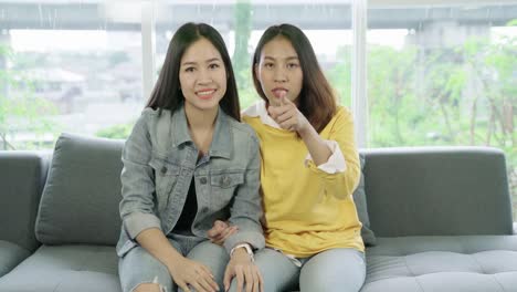 Young-attractive-asian-girlfriends-sitting-together-at-couch-sofa-at-home-smiling-and-watching-TV-show-feeling-happy-lgbt-lesbian.-Beautiful-homosexual-couple-women-or-bestfriends-concept.