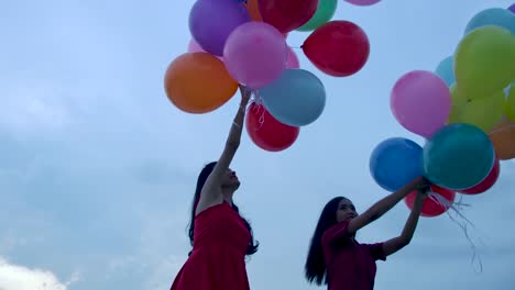 Two-girls-holding-balloon-with-sky-background-in-slow-motion.