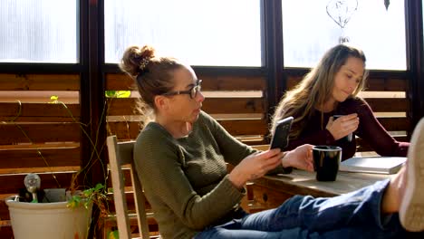 Pareja-de-lesbianas-usando-teléfono-móvil-y-libro-de-lectura-al-mismo-tiempo-que-café-4k