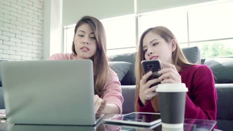 Lesbian-Asian-couple-using-laptop-making-budget-in-living-room-at-home,-sweet-couple-enjoy-love-moment-while-lying-on-the-sofa-when-relax-at-home.-Lifestyle-couple-relax-at-home-concept.