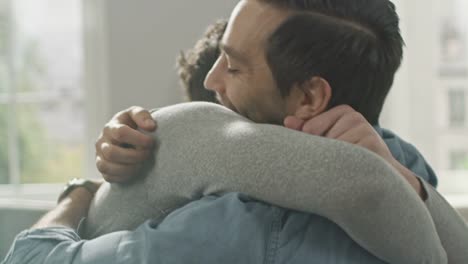 Nette-attraktive-männliche-Gay-paar-sitzen-zusammen-auf-dem-Sofa-zu-Hause.-Freunde-sind-Hugging-und-umarmen-einander.-Sie-sind-glücklich-und-Lächeln.-Sie-sind-lässig-gekleidet-und-Zimmer-ist-Modern-eingerichtet.