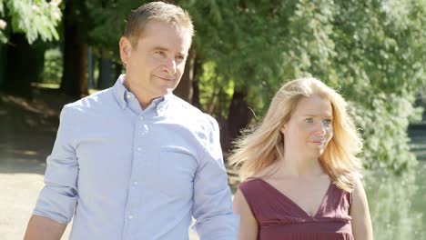 Mature-Couple-On-Their-Way-to-a-Picnic-Look-Out-Over-a-Pond-in-a-Park