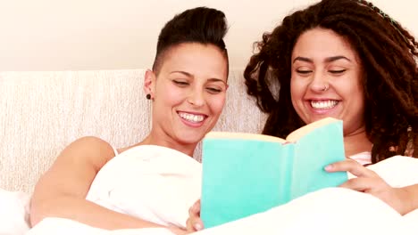 Smiling-lesbian-couple-reading-book-in-the-bed