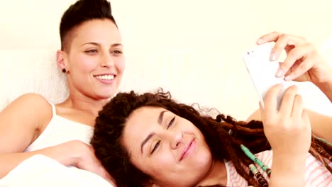 Smiling-lesbian-couple-using-smartphone-together-in-the-bed