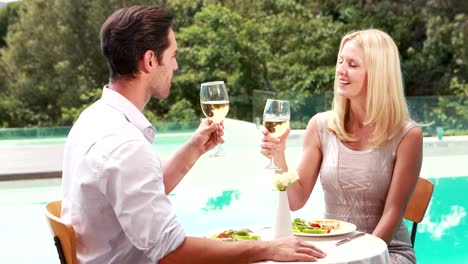 Sonriente-pareja-bebiendo-vino-junto-a-la-piscina