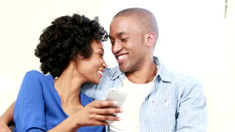 Happy-young-couple-sitting-on-the-couch-while-girlfriend-is-texting