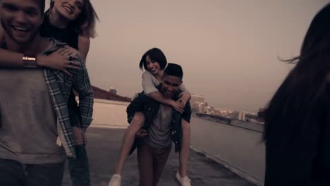 Young-adult-friends-doing-funny-piggyback-rides-on-rooftop