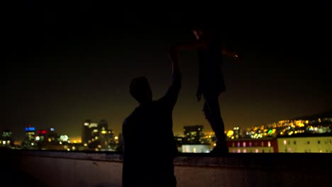 Man-is-holding-hand-with-girlfriend-who-is-balancing-on-rooftop-edge