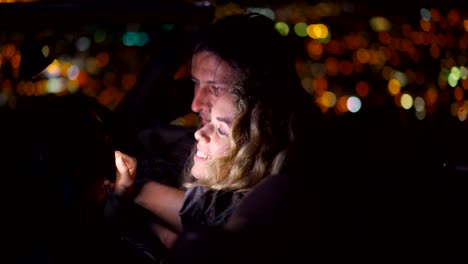 Young-couple-looking-at-pictures-in-a-convertible-at-night