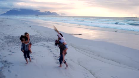 Hipster-friends-having-funny-piggyback-rides-on-beach-at-sunset