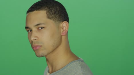 Young-African-American-man-looking-intensely-at-the-camera,-on-a-green-screen-studio-background