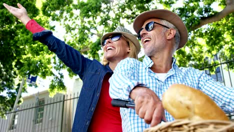 Mature-couple-is-smiling-and-pointing-on-the-same-bike-in-the-street