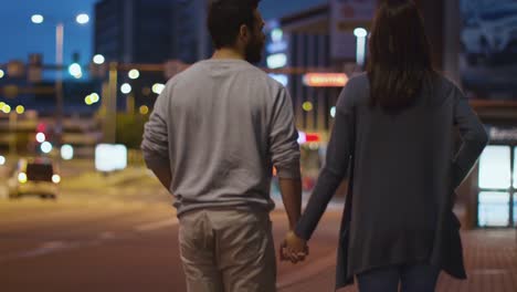 Seguir-a-tiro-de-la-atractiva-pareja-feliz-caminando-por-las-calles-de-la-ciudad-de-noche
