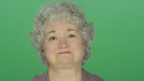 Older-woman-looking-slightly-sad,-on-a-green-screen-studio-background