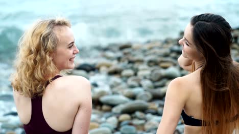 Dos-hermosa-mujer-relajada-y-disfrutar-sobre-el-mar-sentado-en-la-playa-grande-de-piedra-salvaje