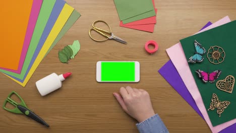 Overhead-Aerial-Footage-Of-Woman-With-Smartphone-And-Craft-Equipment