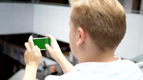 The-guy-plays-the-game-on-the-smartphone-in-shooter-shooter-and-race.-Green-phone-screen-for-keying.-A-man-in-the-building-is-playing-a-smartphone.-Smartphone-turns-on-on-white-background