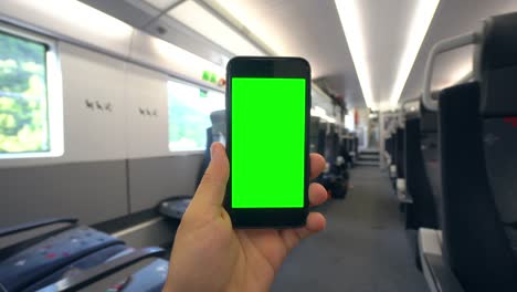 Hand,-die-eine-Handy-mit-einem-Green-Screen-auf-dem-Zug