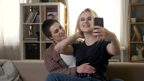 Zwei-junge,-schöne-Mädchen-sitzen-auf-der-Couch-und-machen-Selfies,-Lesben,-LGBT.-60fps