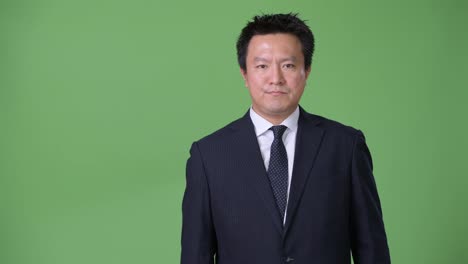 Mature-Japanese-businessman-against-green-background