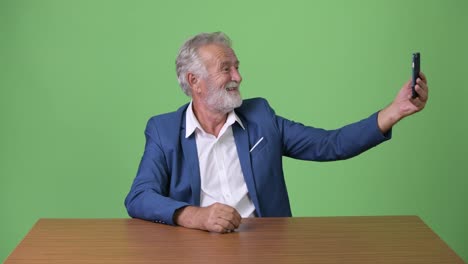 Handsome-senior-bearded-businessman-against-green-background