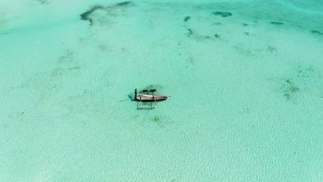 Aerial-view-of-a-fisherman-sails-on-a-wooden-boat-on-clear-blue-water-along-a-tropical-exotic-beach-in-Africa